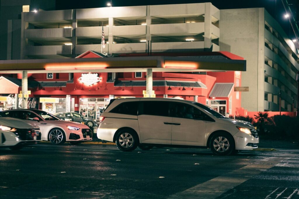 夜のガソリンスタンド。明かりのついた給油所に、車が並んでいる様子